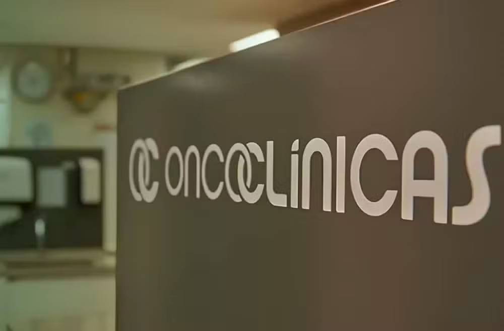 Logo da Oncoclínicas com fundo de gráfico financeiro em queda
